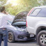 The driver is calling for insurance after a traffic accident. car crash accident on street, damaged automobiles after collision. The car crashed on a road between a saloon and a pickup.