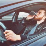 A drunken man driving a car with a bottle of alcohol in his hand. Man whiskey from an iron flask behind the wheel of a car